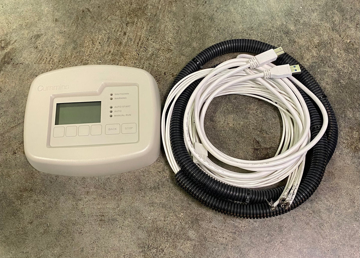 An electronic control module with a small LCD screen and buttons, shown next to a coiled bundle of white cables wrapped in black corrugated tubing on a gray concrete floor.
