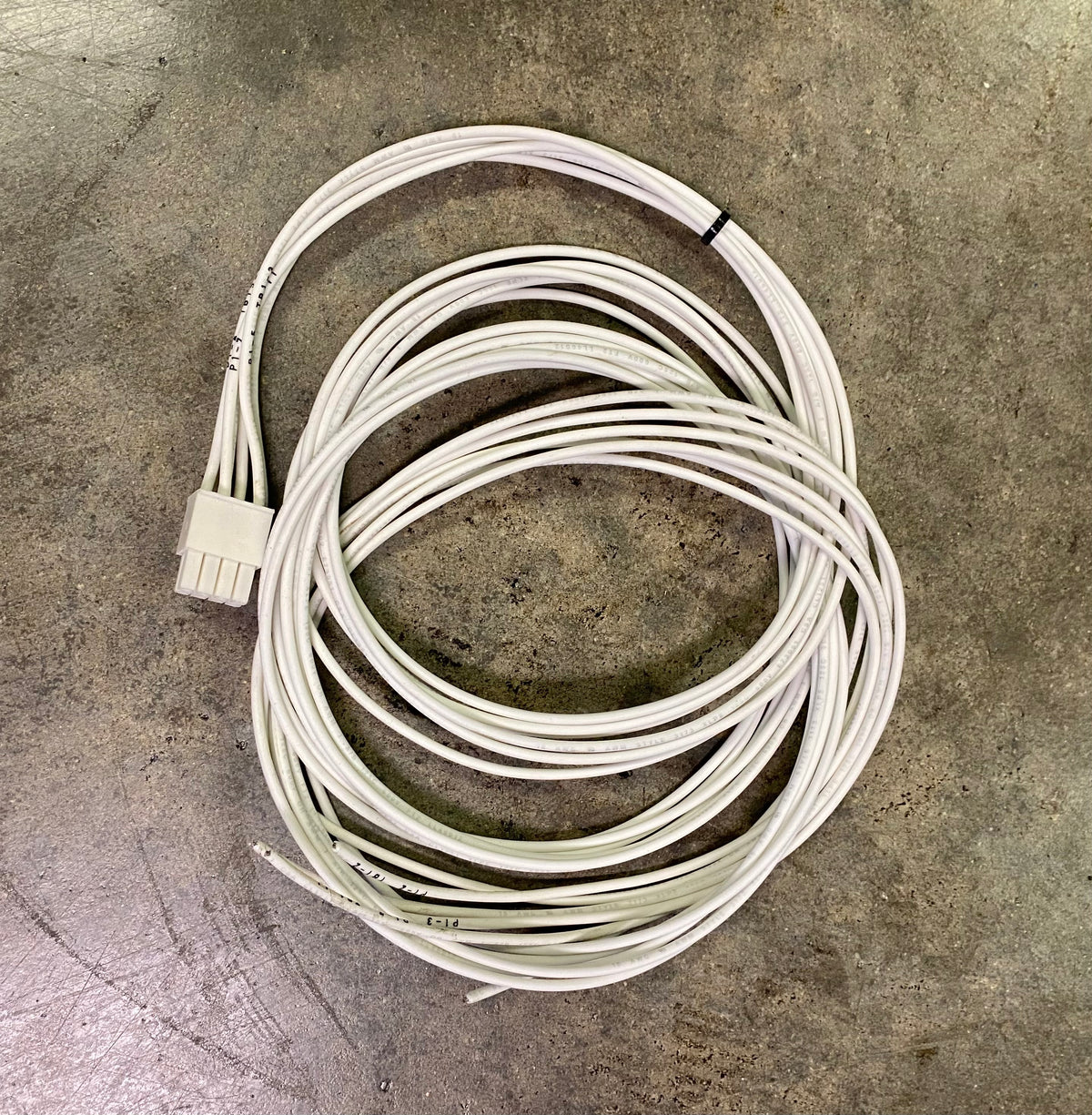 A coiled white multi-pin cable with a multi-pin connector plug, resting on a textured gray concrete floor.