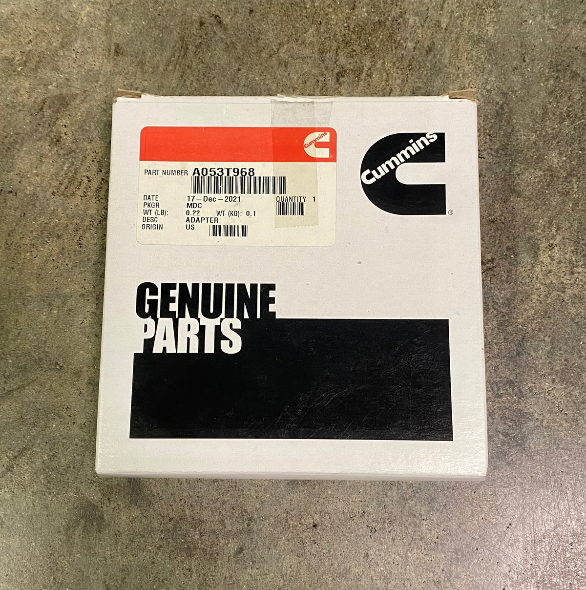 Cummins genuine parts box, part number ADS3T968, on a textured gray concrete floor. The white box features the black Cummins logo and a red and white label.